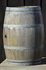 Vintage slate wooden barrel with bit weathered staves surface and galvanized hoops and cylindrical hole in middle where diameter is largest.