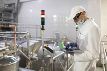 Naklejka premium man in a white robe and a mask with a laptop in his hands is at the factory