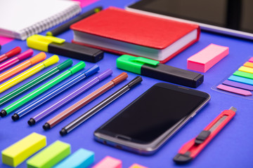 Top view of business desk composite with smartphone, calculator, stickers, and colored pens on pink and blue background