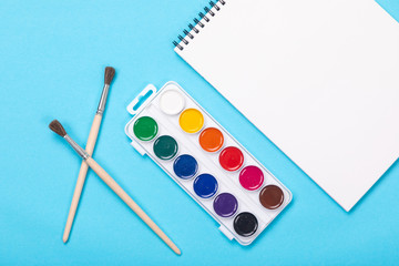 Watercolor paints and brush with album for painting isolated on blue background