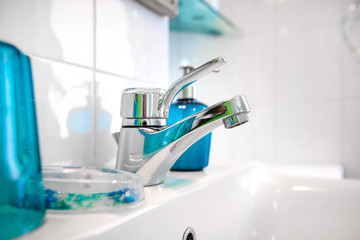 Modern tiled bathroom sink basin faucet paired with blue or turquoise glass soap containers....