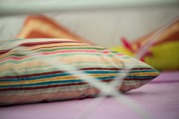 Macro shot of a colorful pillow taken through a modern design style bed. Warm light from lit candles in the background.  