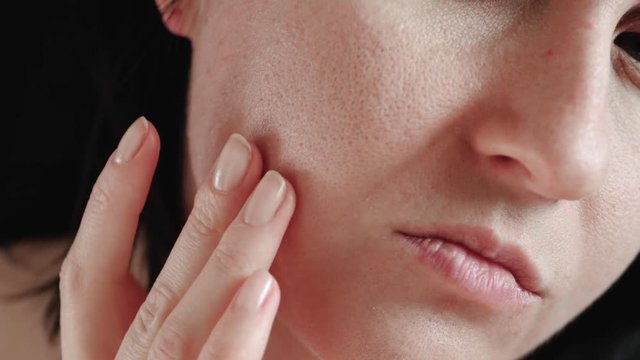 Close-up of a woman's face. The girl touches the fingers of problem skin with enlarged pores, examining it. The concept of caring for problem skin, aging, environmental effects on the skin.