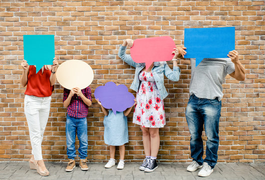 Family holding blank colorful speech bubbles by a brick wall - Powered by Adobe