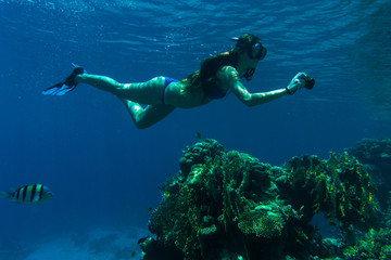 Young woman snorkeling with camera take photo over coral reef in blue sea