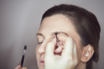 Fototapeta premium Young beautiful woman applying make-up by make-up artist. Process of making makeup.