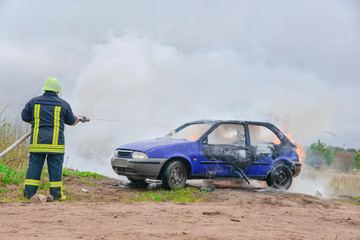 Fototapeta na wymiar Fire fighter prepare to attack a propane fire. Burning and crashed car after explosion. Accident on street at countryside. No one was injured. Artificially created set for film making
