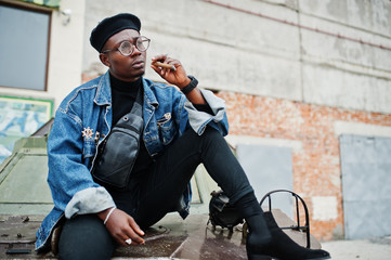 African american man in jeans jacket, beret and eyeglasses, smoking cigar and posed against btr...