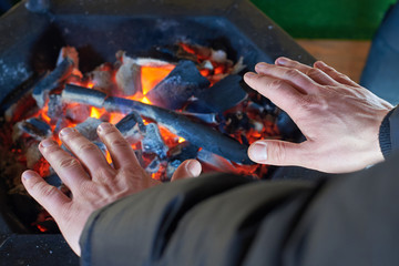 A man is warming his hands on glowing coals