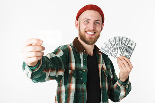 Image of handsome man holding credit card and fan of dollar money, while standing isolated over white background