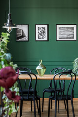 Black and white posters in frames on empty grey wall of fashionable dining room with wooden table...