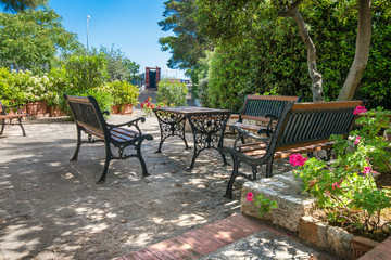 Vintage Italian style garden furniture set up on a terrace next to a villa. Bright red flowers in the front.