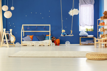 Bright interior of kid's room with blue wall with golden stars and scandinavian wooden bed with...