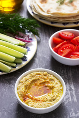 Vegan food, homemade hummus with flatbread, vegetables and olive oil on a concrete background.