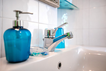 Modern tiled bathroom sink basin faucet paired with blue or turquoise glass soap containers....
