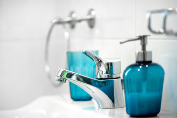 Modern tiled bathroom sink basin faucet paired with blue or turquoise glass soap containers. Concept of cleaning the bathroom.  