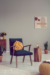 Knot pillow on vintage armchair in grey living room interior