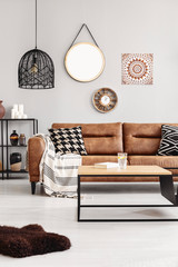 Brown leather couch with blanket and patterned cushions in real photo of bright living room...