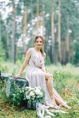 Boudoir photo shoot of the bride in the woods with a bouquet. Flying dress and beautiful girl in the Park.