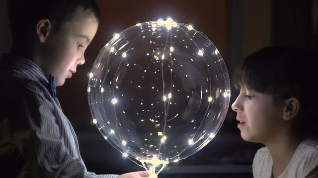 Boy m girl looking through transparent ball. Garland of lights. Dark background. Festive mood. Romantic atmosphere. Close up. Relations. Love.