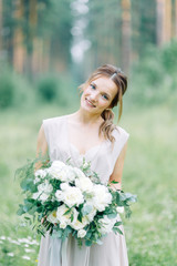 Boudoir photo shoot of the bride in the woods with a bouquet. Flying dress and beautiful girl in the Park.