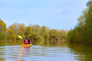 Spring kayaking. Concept for adventure, travel, action, lifestyle. Rear view of kayaker man paddle yellow kayak on Danube river.
