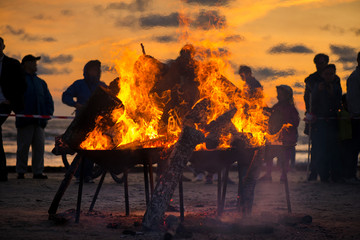 Large burning bonfire with soft glowing flame and sparkles flying all around. Romantic summer evening, people relaxing and enjoying calmness at the seaside during the Night of ancient lights.  
