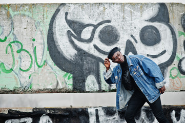 African american man in jeans jacket, beret and eyeglasses against graffiti wall with skull.