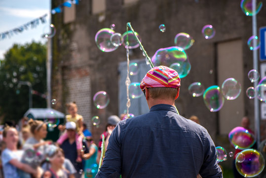 A freelance clown blowing hundreds of tiny, small and big bubbles at outdoor festival in city center. Concept of entertainment, birthdays. Kids having fun. Shower of bubbles flying in the happy crowd