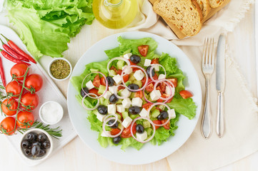 Greek salad on white plate on old rustic white wooden table, fresh salad with tomatoes, cucumbers, feta, onion. Top view