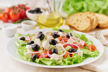 Greek salad on white plate on old rustic white wooden table, fresh salad with tomatoes, cucumbers, feta, onion. Side view, close up