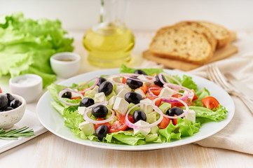 Greek salad on white plate on old rustic white wooden table, fresh salad with tomatoes, cucumbers, feta, onion. Side view, close up