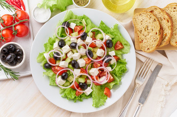 Greek salad on white plate on old rustic white wooden table, fresh salad with tomatoes, cucumbers, feta, onion. Top view