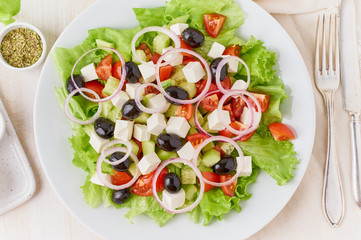 Greek salad on white plate on old rustic white wooden table, fresh salad with tomatoes, cucumbers, feta, onion. Top view
