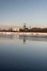 Fototapeta na wymiar headframe od Ful Darkov bituminous coal mine reflecting on water fround of Karvinske more lake near Karvina city in Czech republic