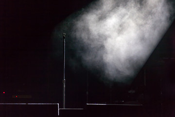 Microphone holder standing on a black dark scene, smoke illuminated by white spotlight at the side,...