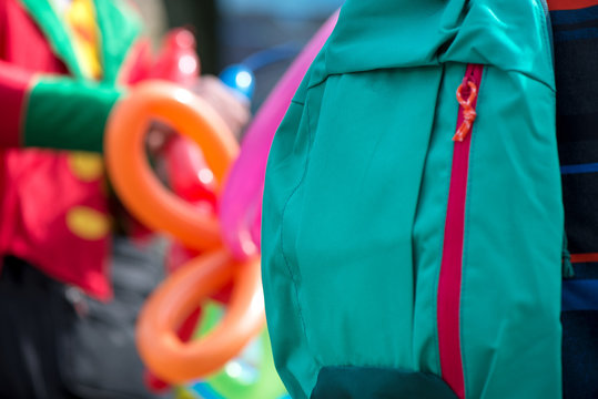 Close up shot of green school backpack. A freelance clown creating balloon animals and different shapes at outdoor festival in city center in the background. Concept of surveillance and stealing  