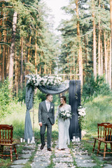 Wedding ceremony at the arch with pine forest in the style of fine art. Beautiful couple and traditions at a wedding in Europe.