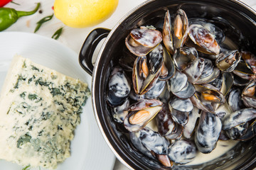 mussels in cheese sauce dor blu, in a black saucepan. On a white wooden background, decorated with...