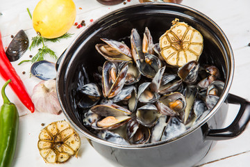 mussels in garlic sauce. in a black pan. On a white wooden background, the background is decorated with vegetables.