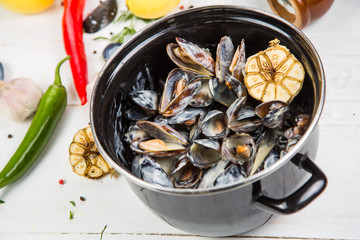 mussels in garlic sauce. in a black pan. On a white wooden background, the background is decorated with vegetables.