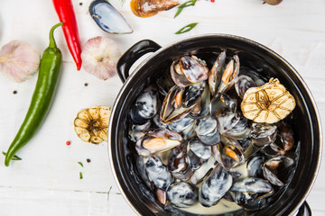mussels in garlic sauce. in a black pan. On a white wooden background, the background is decorated with vegetables.