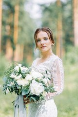 The bride in a wedding dress in nature with a bouquet. Boudoir photo shoot in pine lemu in the style of fine art.