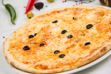 Margarita pizza with black olives on white wooden background. The background is decorated with vegetables.