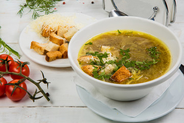 onion soup in a white plate with crackers on a white wooden background. The background is decorated with vegetables.