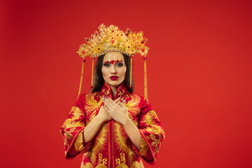 Fototapeta premium Chinese traditional graceful woman at studio over red background. Beautiful girl wearing national costume. Chinese New Year, elegance, grace, performer, performance, dance, actress, dress concept