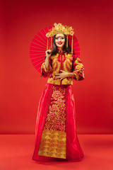 Fototapeta na wymiar Chinese traditional graceful woman at studio over red background. Beautiful girl wearing national costume. Chinese New Year, elegance, grace, performer, performance, dance, actress, dress concept