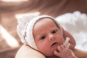 Portrait of newborn baby in white hat, eyes squint