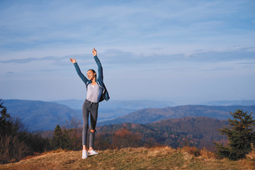 happy woman hiker standing on edge of mountain ridge against background of sunset