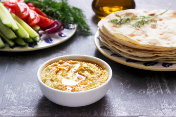 Vegan food, homemade hummus with flatbread, vegetables and olive oil on a concrete background.